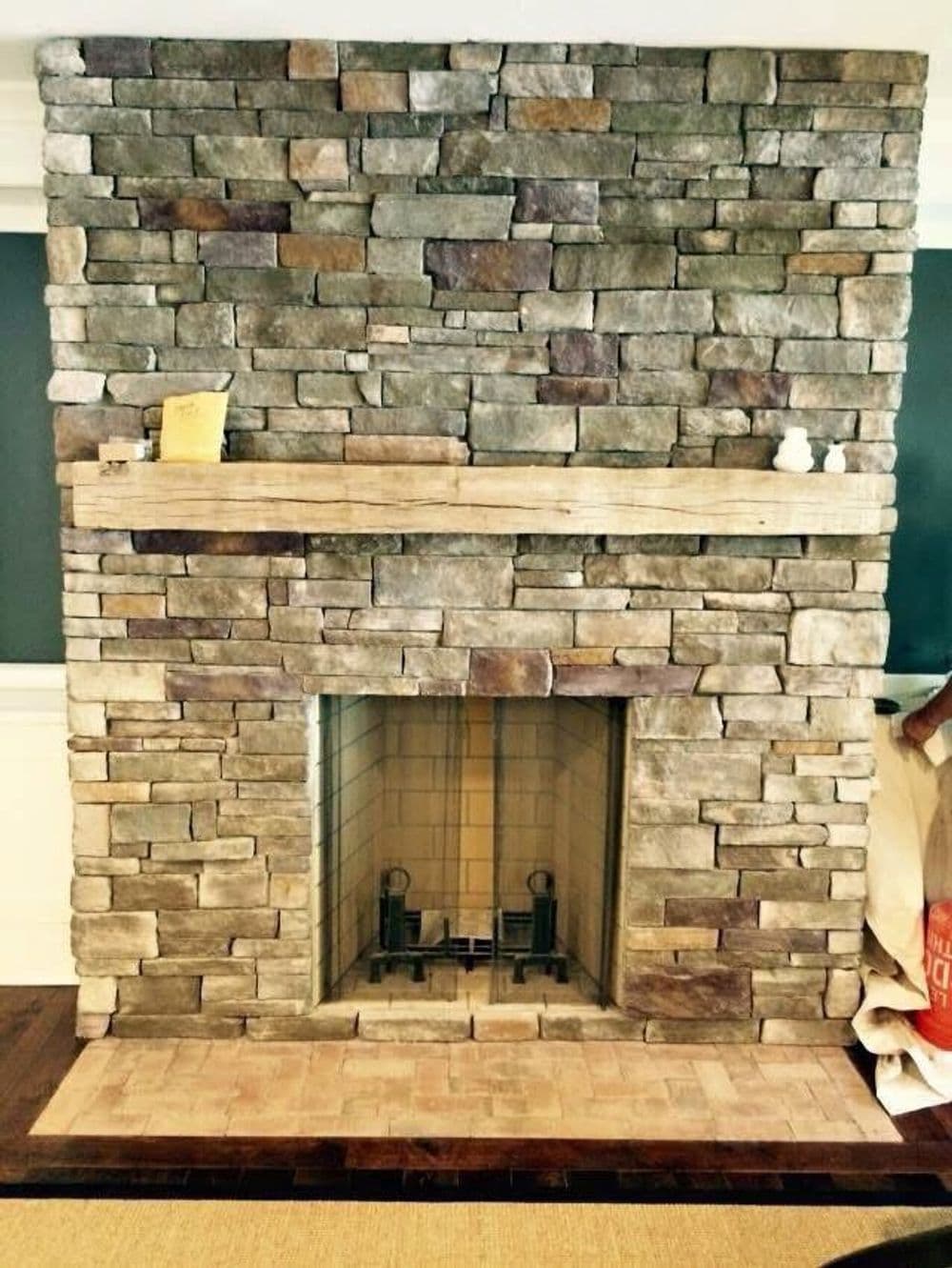 Natural stone fireplace with wooden mantel and brick hearth in modern living room.